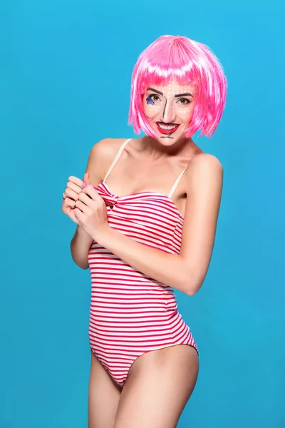 Jeune femme avec du pop art créatif maquillage et perruque rose regardant la caméra sur fond bleu — Photo