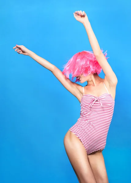 Jeune femme avec du pop art créatif maquillage et perruque rose regardant la caméra sur fond bleu — Photo