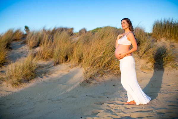 Donna incinta in piedi sulla spiaggia al tramonto — Foto Stock