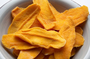 Kurutulmuş mango dilimleri bir kasede. Arka plan, mutfak, sağlıklı, atıştırmalık, meyve, beslenme, stüdyo ışığı, egzotik, Vietnam ürünleri, doğal, vegan, vejetaryen, şeker, sigarsız