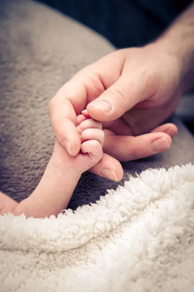 Evde korunmak için annesinin elini ve parmağını tutan küçük bir bebek.