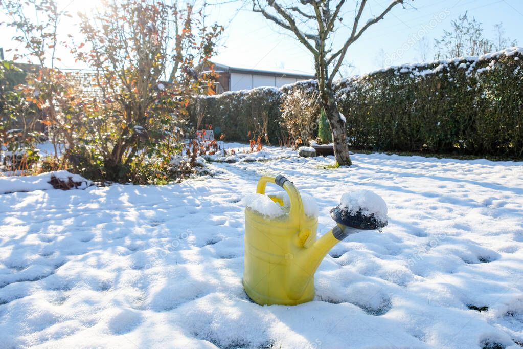 A yellow watering can stands in the snow-covered garden in winter