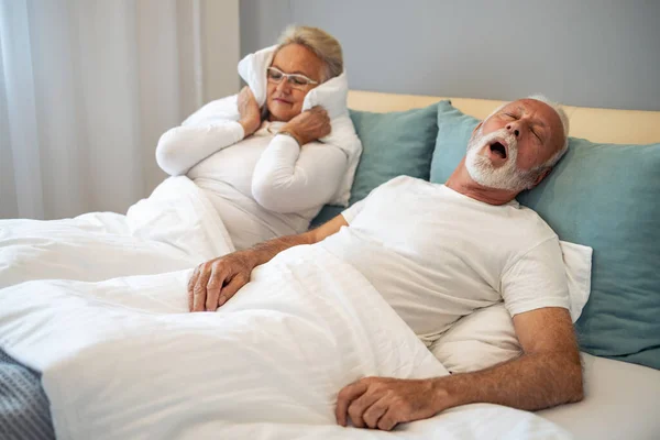 Kocası horladığı için kulaklarını tıkayan stresli yaşlı bir kadın. Yaşlı çiftin horlamasıyla ilgili sorunları var..