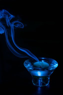 Koyu arkaplan ve söndükten sonra mumdan çıkan dumanla birlikte mavi cam mum tutacağı..