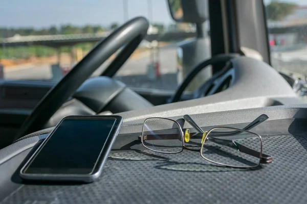 Glasses and mobile phone on the dashboard of a truck.