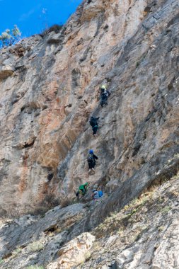 Taşın içine metal zımbalar yerleştirilmiş kayalık bir duvara tırmanan birkaç kişi var. Buna Via Ferrata da deniyor..
