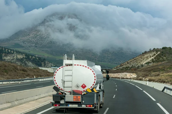 Small tank truck for home fuel delivery driving on the highway with views of mountains with clouds around it.