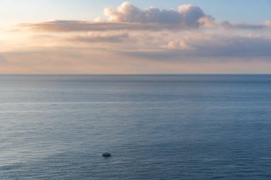 Büyük denizin önündeki küçük tekne, şafak vakti gökyüzünde bulutlar..