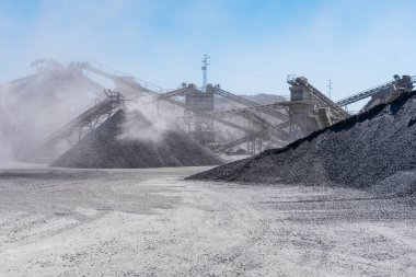 Arid quarry with moving mechanical belt line to separate gravel by size, all wrapped in a cloud of dust.