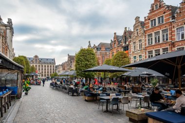 Leuven, Belçika - 12 Ekim 2025: Oude Markt 'ta açık kafeler, yemek yiyen insanlar ve bulutlu bir gökyüzü altında tarihi Flaman cepheleri ile dolu bir atmosfer.