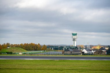Brüksel Havalimanı 'ndaki (Zaventem) kontrol kulesi, kapalı bir gökyüzü altında pist ve çevre üzerinde yükseliyor.