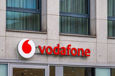 Aachen, Almanya - Aralık 04, 2025: Vodafone logosu ve marka tabelası şehir merkezindeki telekomünikasyon perakendeciliğini gösteren pencereli modern bir taş cepheye monte edildi.