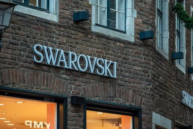Aachen, Almanya - 04 Aralık 2025: Aachen şehir merkezindeki tarihi tuğla cephesine asılan Swarovski mağaza tabelası, kentsel bir ortamda lüks bir perakende markasını gösteriyor.