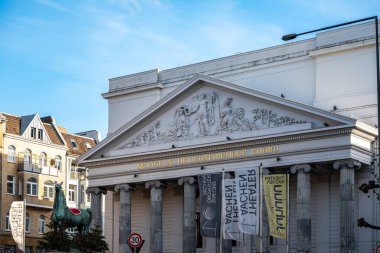 Aachen, Almanya - 04 Aralık 2025: Aachen Tiyatrosu 'nun Neoklasik cephesi yontulmuş bebek ve sütunlarıyla, gündüz gözüyle pankartlar ve kentsel çevrelerle görülüyor.