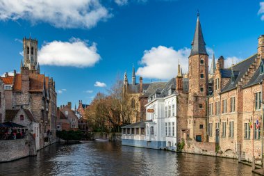 Bruges, Belçika - 14 Şubat 2026: Rozenhoedkaai 'nin ortaçağ tuğla evleri ve Brüksel' in tarihi merkezinde kanal boyunca çan kulesi bulunan ikonik manzarası.