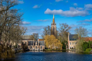 Bruges, Belçika - 14 Şubat 2026: tarihi Sashuis ve Leydimizin Kilisesi 'nin Brüksel' deki ortaçağ evlerinin üzerinde yükseldiği Minnewater Gölü manzarası.