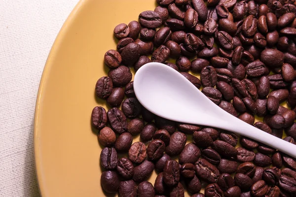 Beyaz Sarı kaşık kahve çekirdekleri ile bir plaka üzerinde