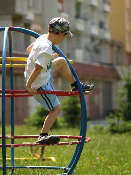 Pojken klättrar på klätterställningar på lekplatsen — Stockfoto