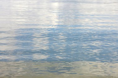 Arka plan, küçük dalgalarla sakin mavi su yüzeyi. Denizin yüzeyinde ya da gölde yansıması