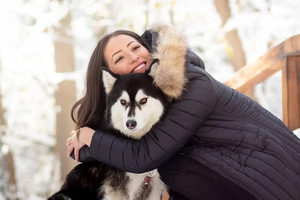 Güzel genç bir kadın soğuk kış gününde dişi köpeğe sarılıyor.