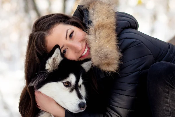 Güzel genç bir kadın soğuk kış gününde dişi köpeğe sarılıyor.
