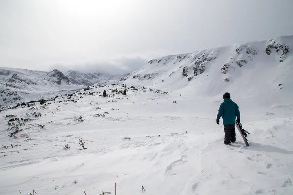 Snowboardcu dağa bakıyor ve koşuşturmaya hazırlanıyor. Bulagaria 'nın Rila dağında kötü fırtınalı hava. Yedi Rila Gölü.