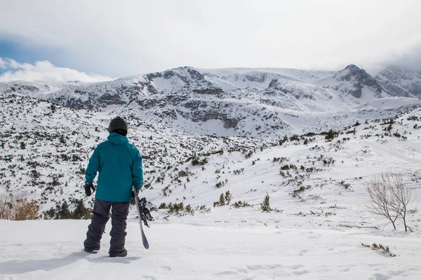 Snowboardcu dağa bakıyor ve koşuşturmaya hazırlanıyor. Bulagaria 'nın Rila dağında kötü fırtınalı hava. Yedi Rila Gölü.