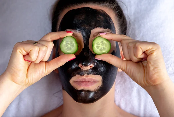 Přirozeně vypadající dívka s černou caracol tvář maska ležící na bílém ručníku v lázeňském salonu — Stock fotografie