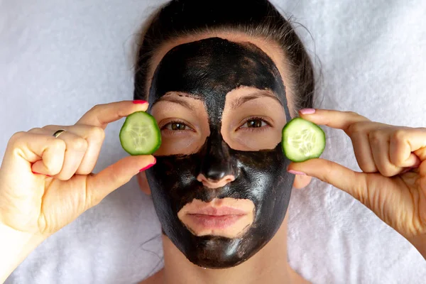 Natuurlijk ogende meisje met zwart caracol gezicht masker leggen op witte handdoek in spa salon Stockfoto
