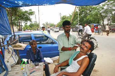 Delhi,India - July 9, 2004: Indian man getting his shave from the roadside shop.