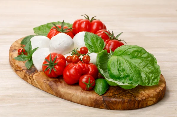 Mozzarella, tomates herederos, hojas de albahaca en una porción de madera — Foto de Stock