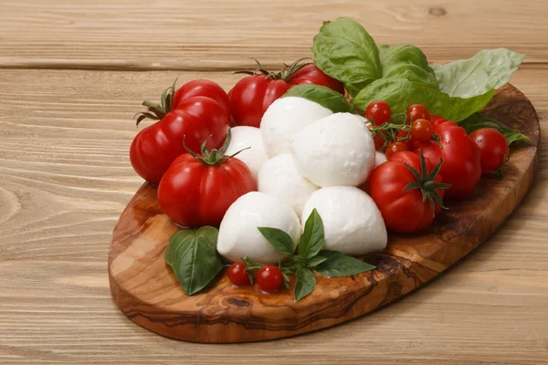 Mozzarella, Tomaten, Basilikumblätter auf einer hölzernen Portion — Stockfoto