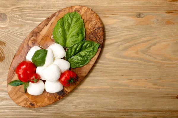 Mozzarella, tomates de herança, folhas de manjericão em uma porção de madeira — Fotografia de Stock