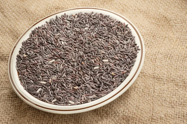 Closeup of raw rice berry inside whole bowl over agriculture sack background