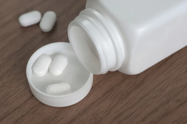 Macro de pastillas en la tapa con la botella de la píldora como fondo — Foto de Stock