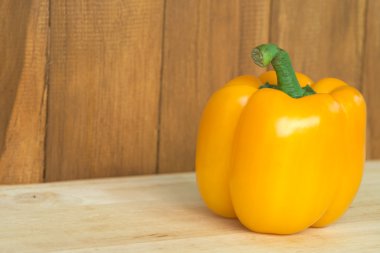 Ahşap masa ve kahverengi ahşap zemin üzerinde tek sarı dolmalık biber