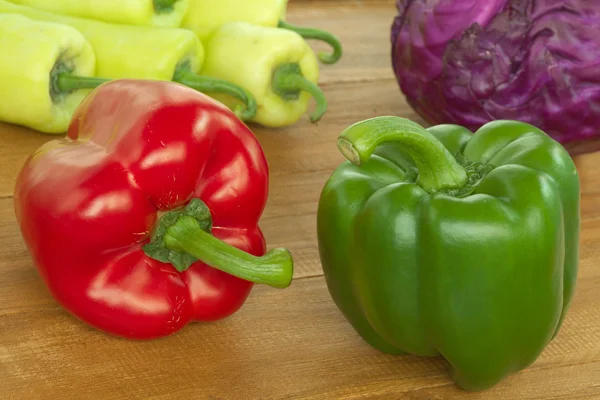 Pimiento rojo y verde sobre mesa de madera con pimiento dulce y repollo rojo fondo — Foto de Stock