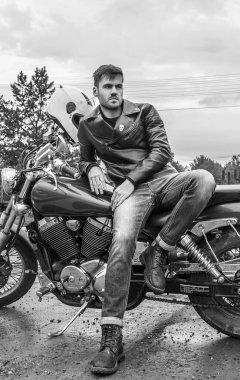 Klasik bir motosikletin üstünde oturan genç bir motosikletçi.