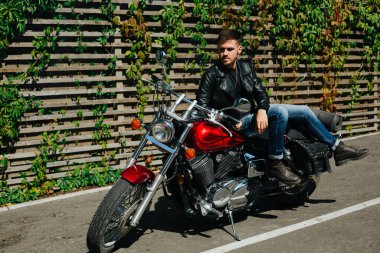 Klasik bir motosikletin üstünde oturan genç bir motosikletçi.