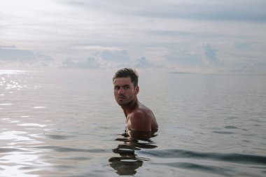 Yakışıklı bir adam sahilde suyun ortasında duruyor.