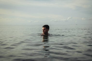 Yakışıklı bir adam sahilde suyun ortasında duruyor.