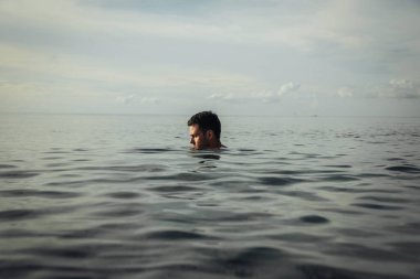 Yakışıklı bir adam sahilde suyun ortasında duruyor.