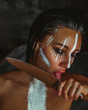 Esmer bir kız tehlikeli bir şekilde bıçağın bıçağını yalıyor.