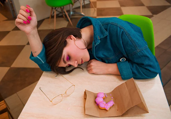 Ένα κορίτσι τρώει ένα ντόνατ σε ένα εμπορικό κέντρο, ακουμπώντας σε ένα τραπέζι — Φωτογραφία Αρχείου
