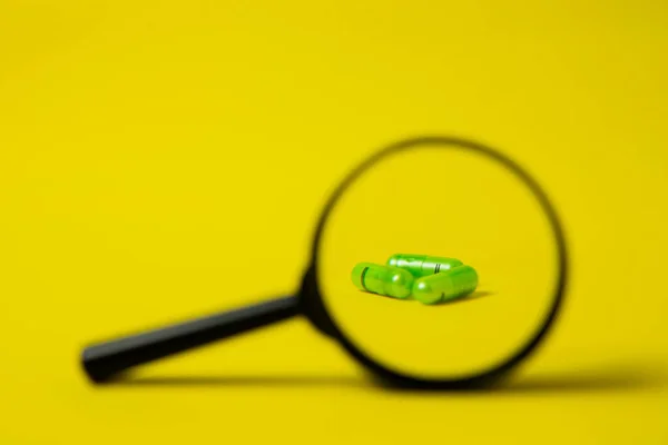 Capsule sotto una lente d'ingrandimento su fondo giallo. Farmacia minima, antibiotici — Foto Stock