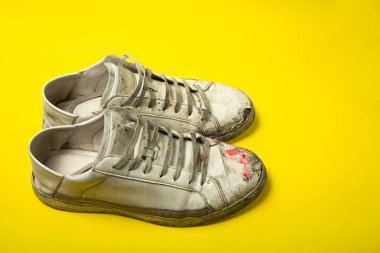Kirli ayakkabılar, sarı arka planda izole edilmiş eski beyaz yırtık ayakkabılar..