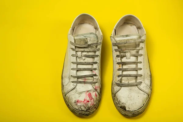 Sapatos sujos, tênis rasgados brancos vintage isolados em um fundo amarelo. — Fotografia de Stock