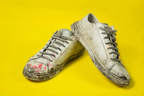 Sapatos sujos, tênis rasgados brancos vintage isolados em um fundo amarelo. — Fotografia de Stock