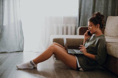 Kız evde dizüstü bilgisayarına bakıyor ve telefonla konuşuyor.