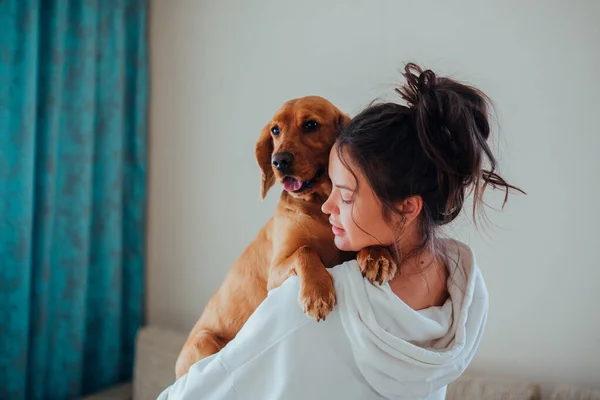 Uma mulher em casa tem um cão nos braços — Fotografia de Stock